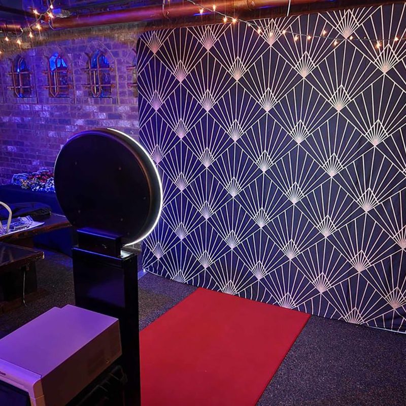 A modern photo booth with a ring light and a black and gold art deco backdrop, set up with a red carpet at an event in Jacksonville, Florida.